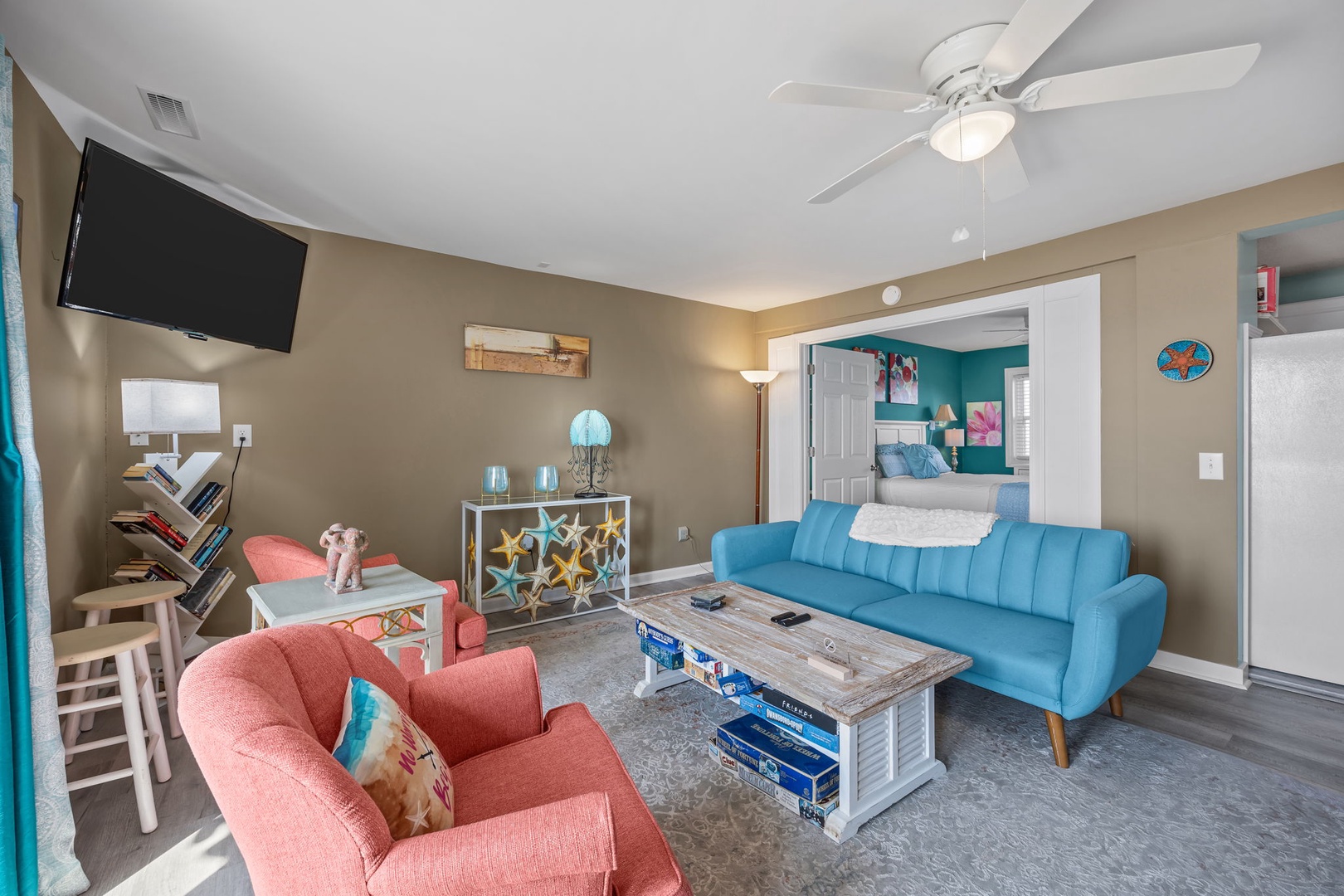 Unwind in your bright living room with plush coral and teal seating, ceiling fan comfort, and flat-screen entertainment after beach days.