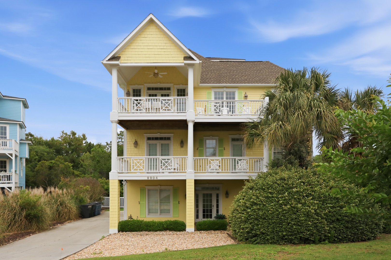 Charming three-story coastal property featuring multiple private balconies, surrounded by lush landscaping and tropical palms in a peaceful residential setting near the beach.