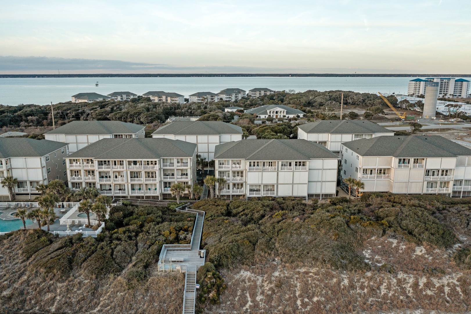 Coastal resort buildings nestled among natural dunes with ocean views and beach access via elevated walkway.