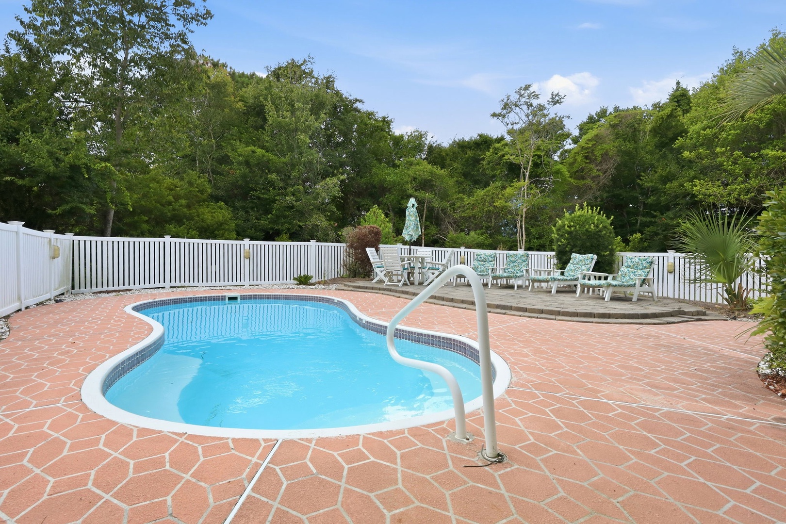 Private freeform pool surrounded by patterned terracotta pavers, lush greenery, and inviting lounge chairs—your perfect spot to soak up the sun and unwind.