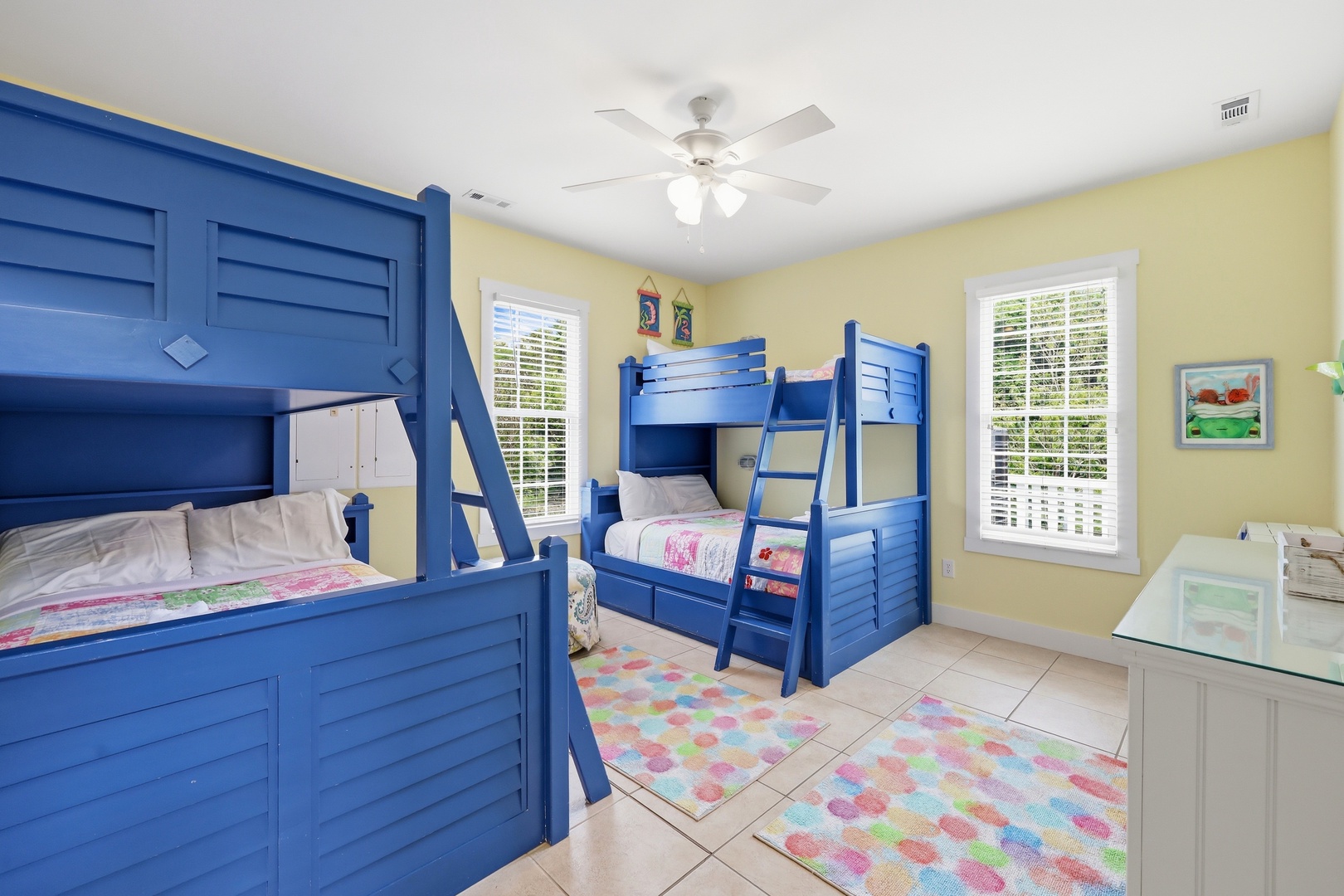 Your kids will love this cheerful room with vibrant blue bunk beds and sunny yellow walls. Soft rugs underfoot and a ceiling fan overhead make their space cozy and comfortable.