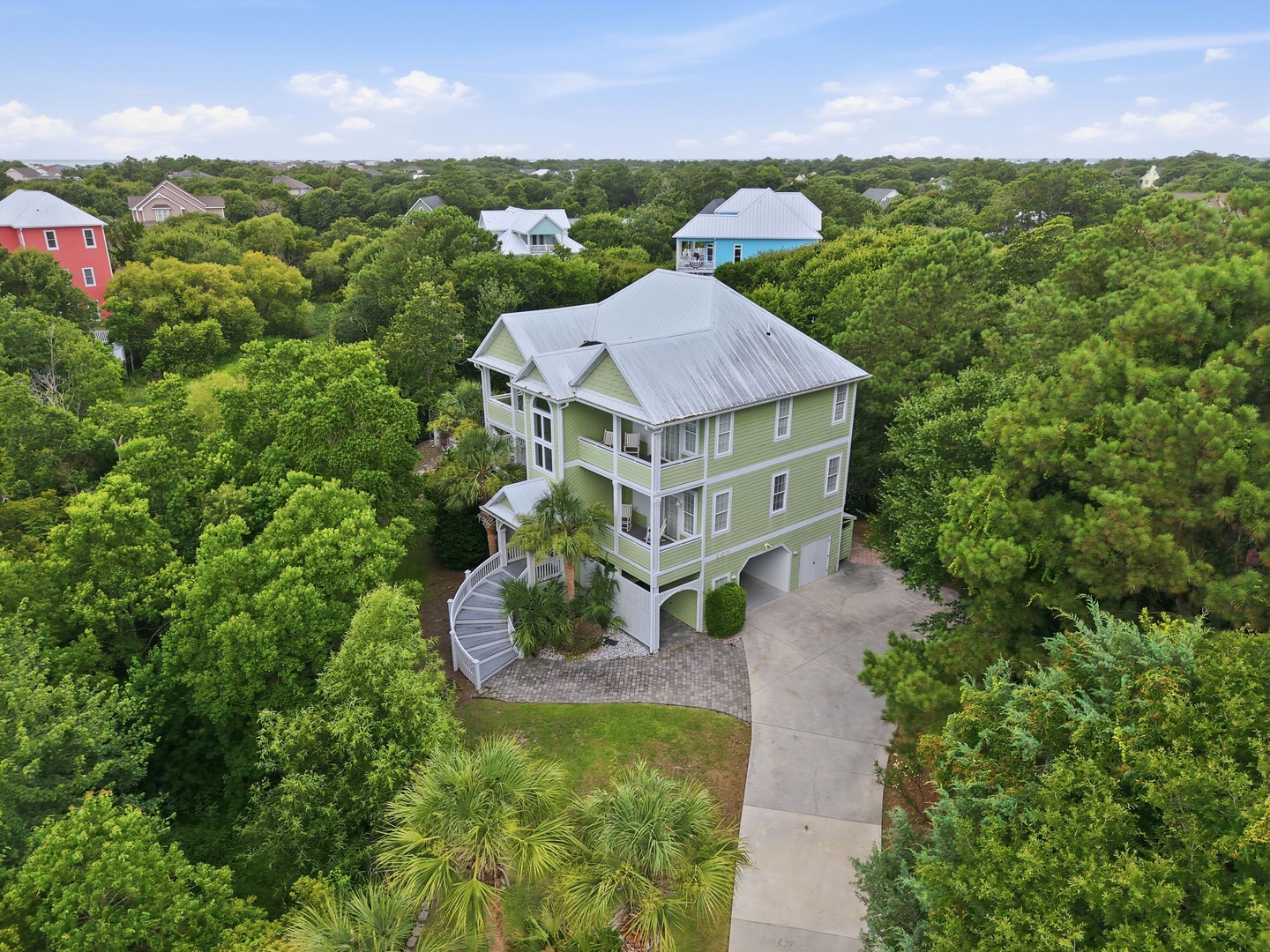 A spacious three-story coastal home nestled among lush greenery, featuring a covered entrance, ample parking, and a peaceful neighborhood setting with nearby beach access.