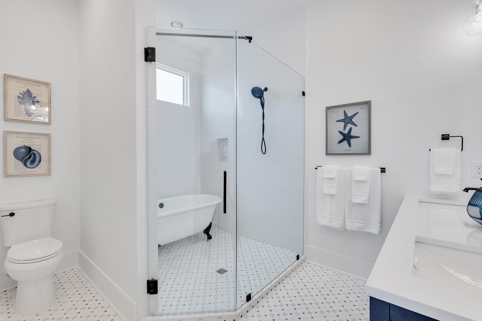 Refresh in your spa-like bathroom with a spacious glass-enclosed shower and vintage clawfoot tub. Crisp white towels and coastal artwork create a serene retreat.