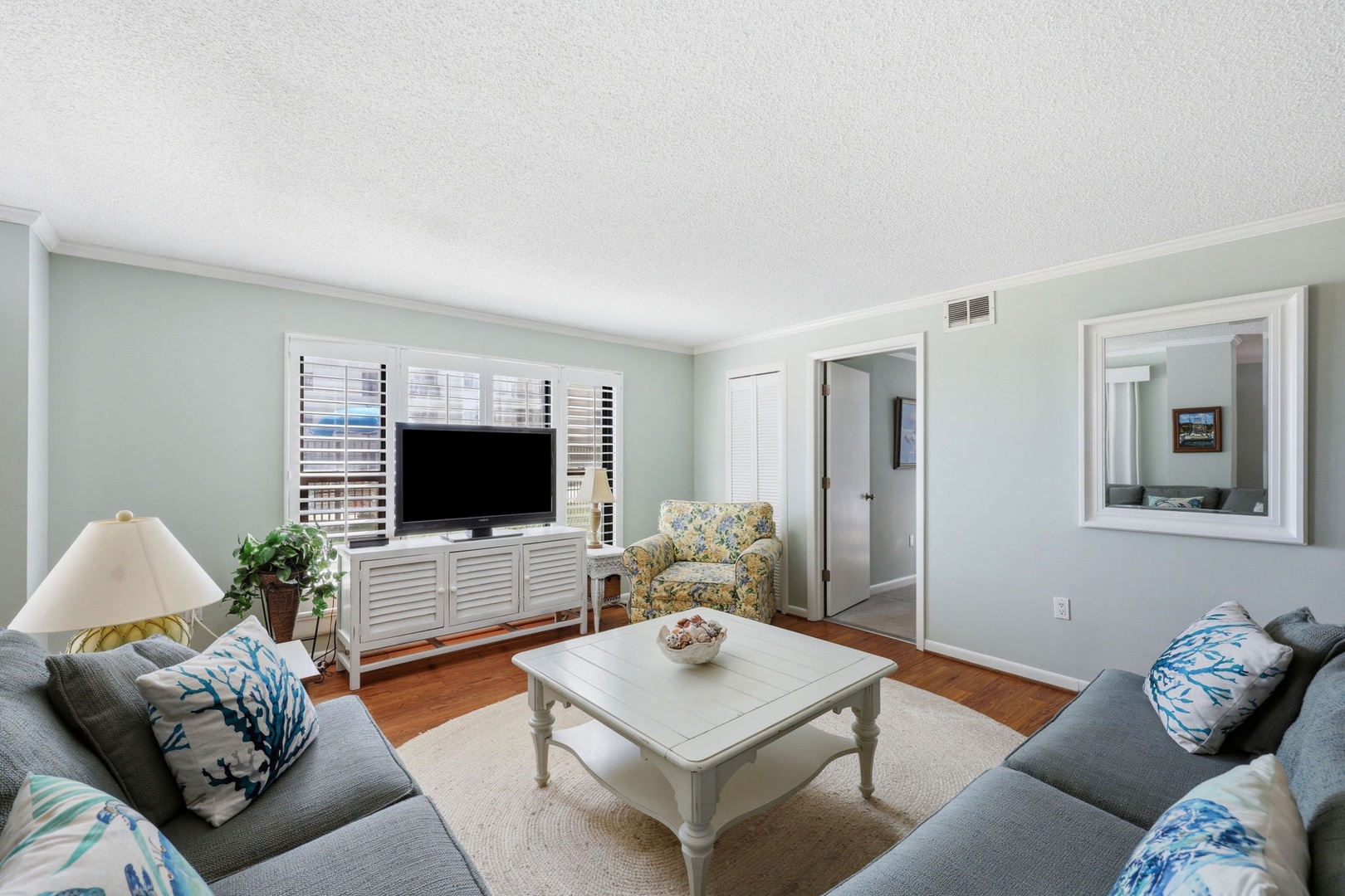 Relax in your bright, coastal-inspired living room with plush seating, hardwood floors, and cheerful décor—perfect for unwinding after a day at the beach.