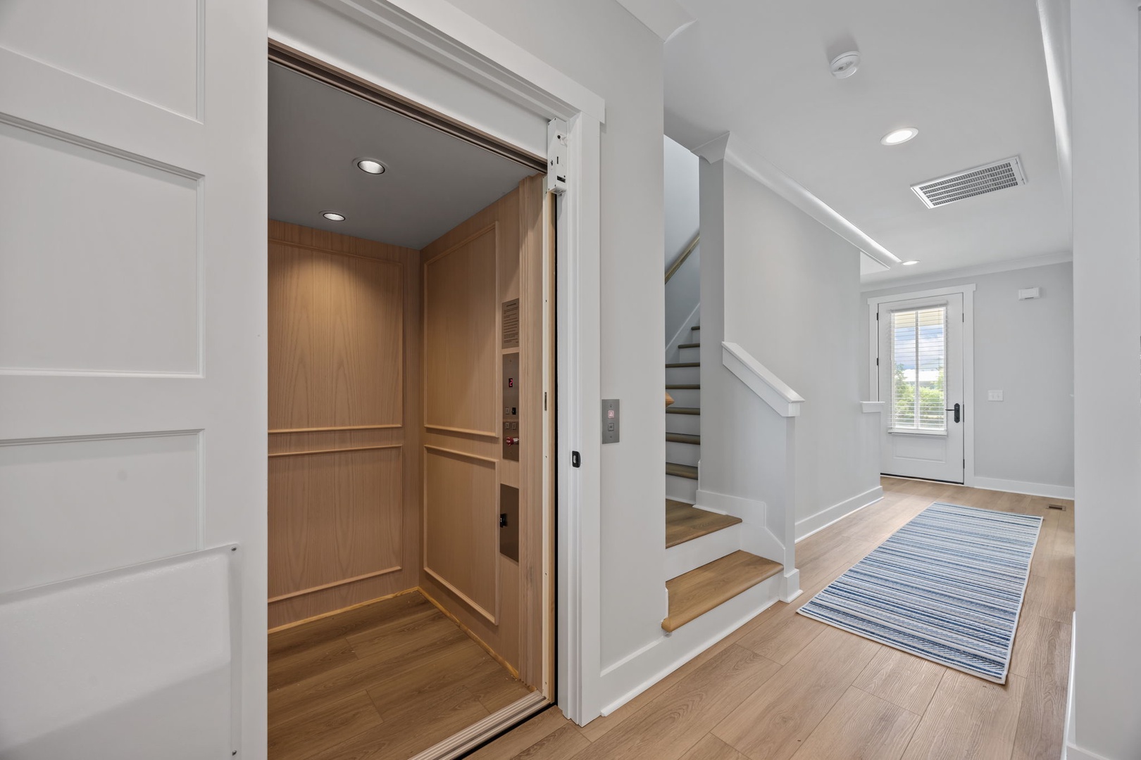 Step into your bright, modern entryway featuring warm hardwood floors, elegant white trim, and convenient elevator access for effortless movement.