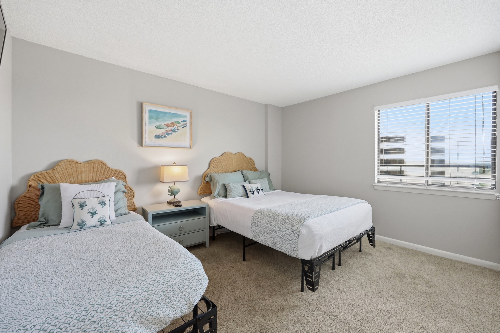 Your bright, coastal-inspired bedroom features two plush beds with natural wicker headboards and soft linens. Wake to natural light streaming through your window, with charming beach-themed decor adding a serene, beachy ambiance.