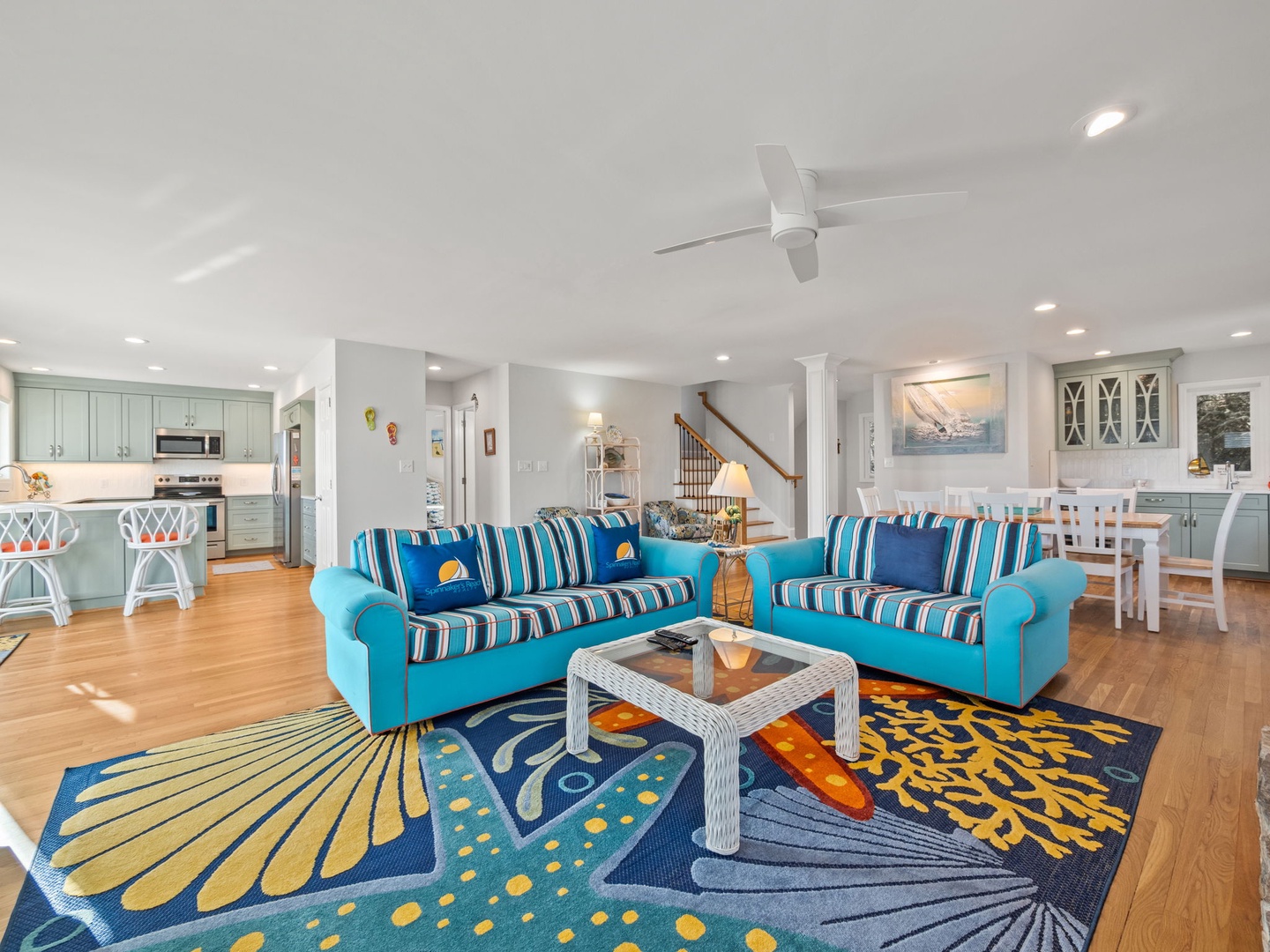 Relax in your vibrant open-concept living space with cheerful blue sofas, coastal-themed decor, and a fully equipped kitchen perfect for family gatherings.