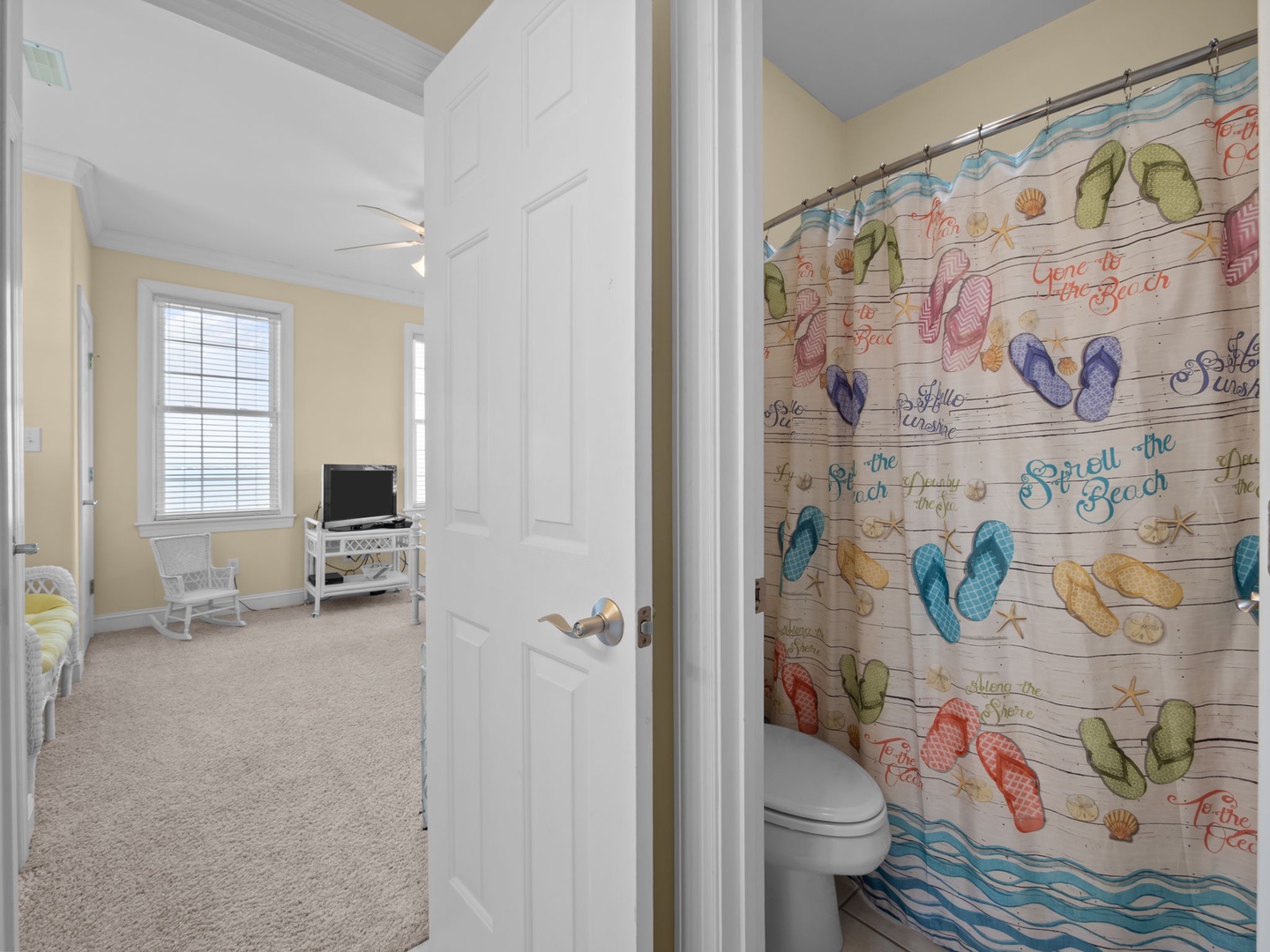 Your private bathroom features a whimsical beach-themed shower curtain, while your cozy bedroom awaits with comfortable seating and entertainment nearby.