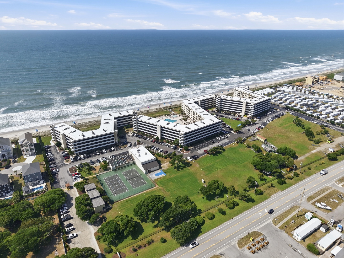Aerial view of a beachfront resort complex featuring tennis courts and green spaces, nestled along a pristine sandy coastline with rolling waves and open ocean beyond.