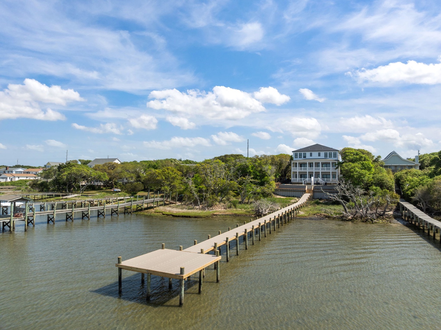 Stunning waterfront property with private dock stretches into calm waters, surrounded by lush coastal landscape and blue skies.
