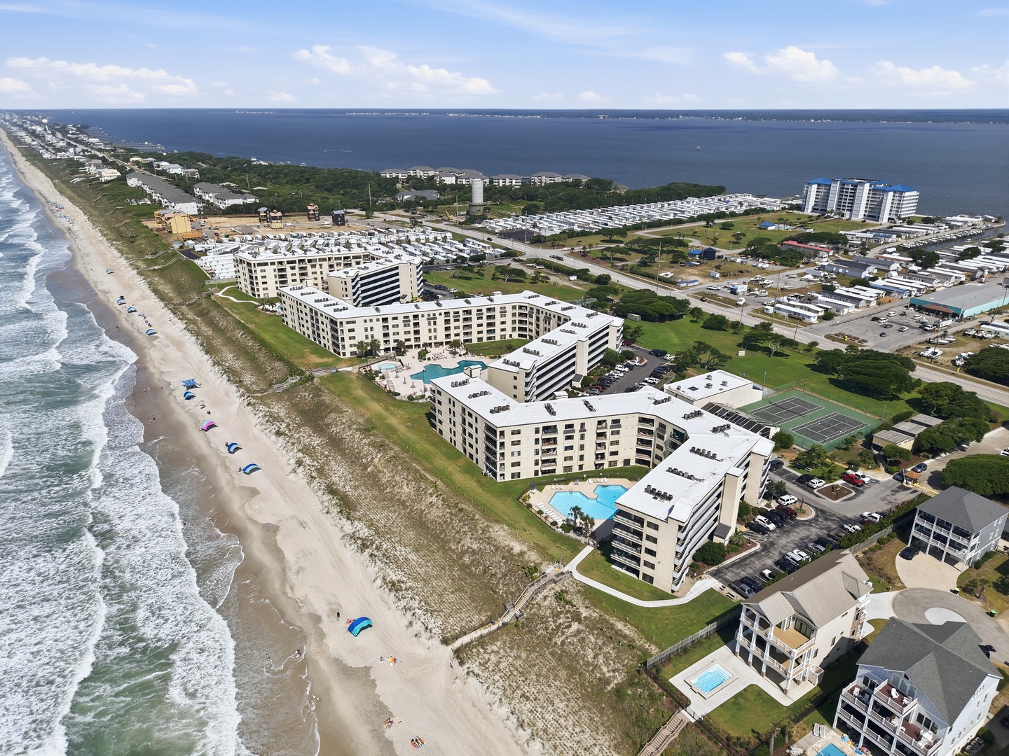 Beachfront vacation rental complex featuring multiple buildings, swimming pools, and tennis courts, with direct beach access along the Atlantic coastline and waterway views.