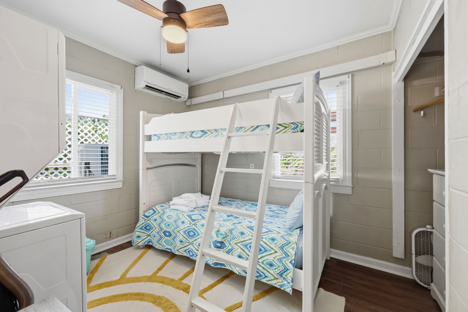 Your coastal-chic bunkroom offers a cheerful retreat with bright white shiplap, vibrant bedding, and a ceiling fan to keep you cool. Large windows flood the space with natural light, while the AC ensures comfort.