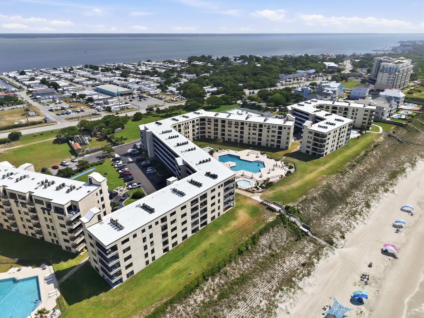 Beachfront resort complex featuring modern buildings, swimming pool, and convenient access to sandy shores along a scenic coastal area.