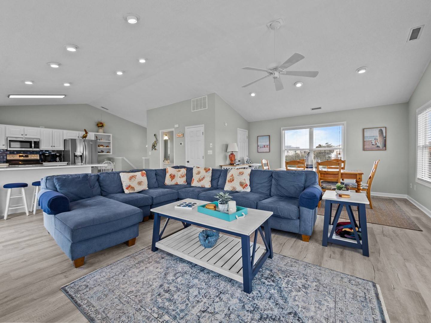 Unwind on your spacious sectional in this open-concept retreat, where coastal blues meet modern comfort beneath soaring ceilings and natural light.