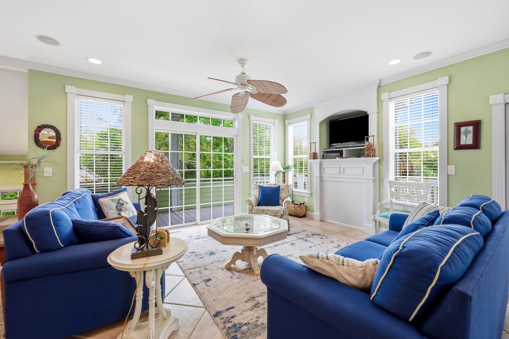 Sink into plush blue sofas beneath a breezy ceiling fan as natural light pours through French doors. Your coastal-chic living room invites relaxed evenings with garden views and modern entertainment.
