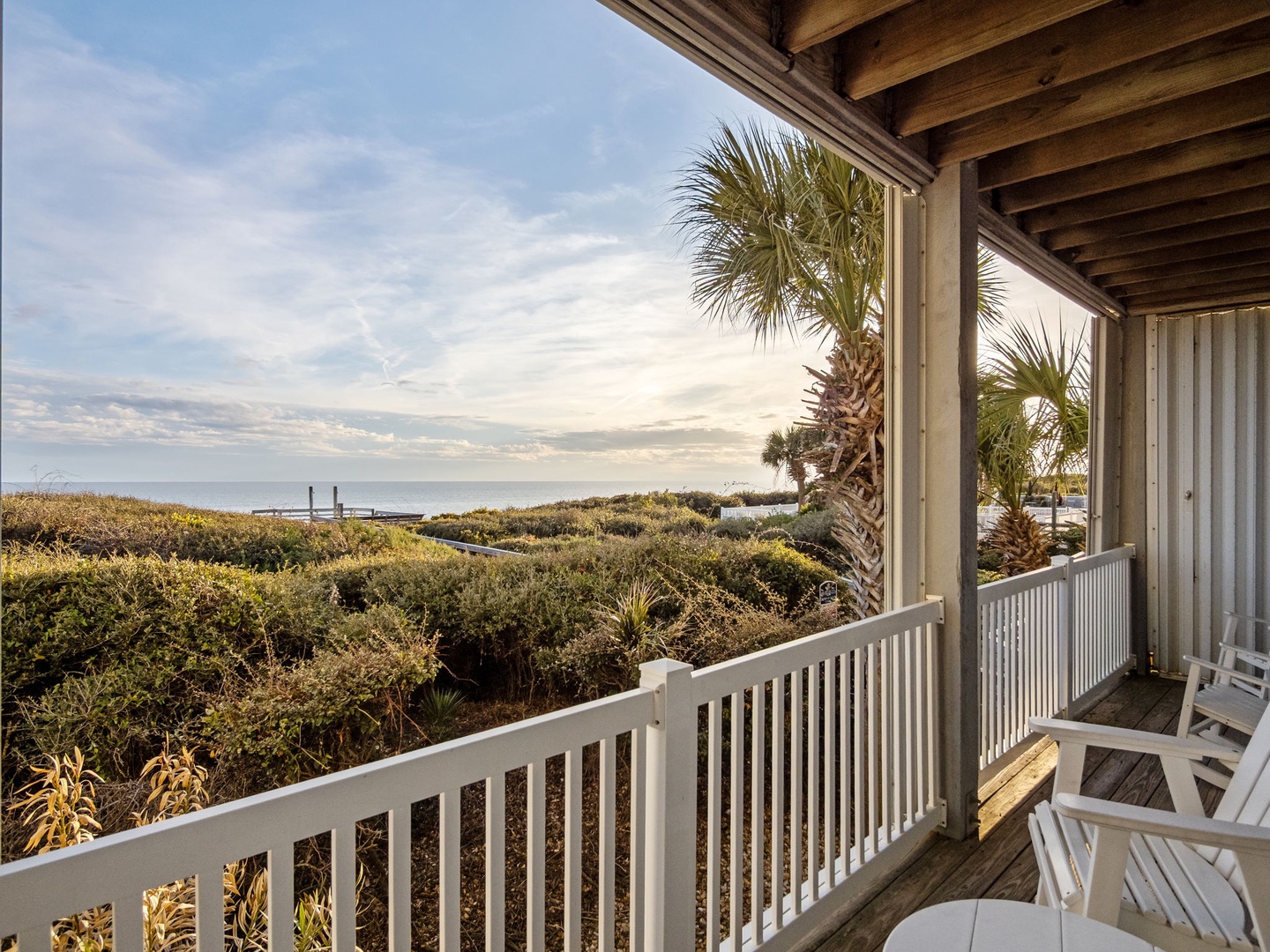 Covered deck with coastal views featuring natural dunes, palm trees, and distant water glimpses through tropical vegetation.