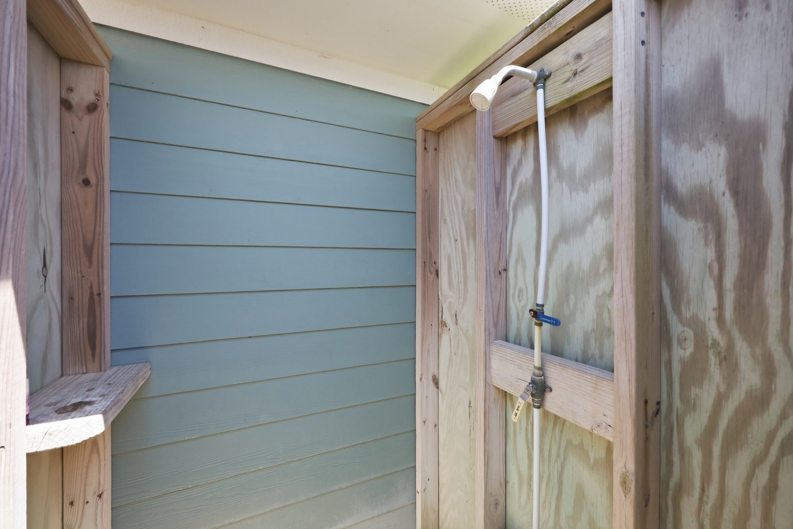 Simple outdoor shower with bench and painted shiplap wall—perfect for rinsing off sand and salt after a day at the beach.