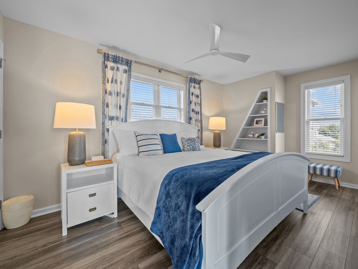 Unwind in your peaceful bedroom sanctuary with coastal-inspired blues, warm lamps, and a ceiling fan for ultimate comfort.
