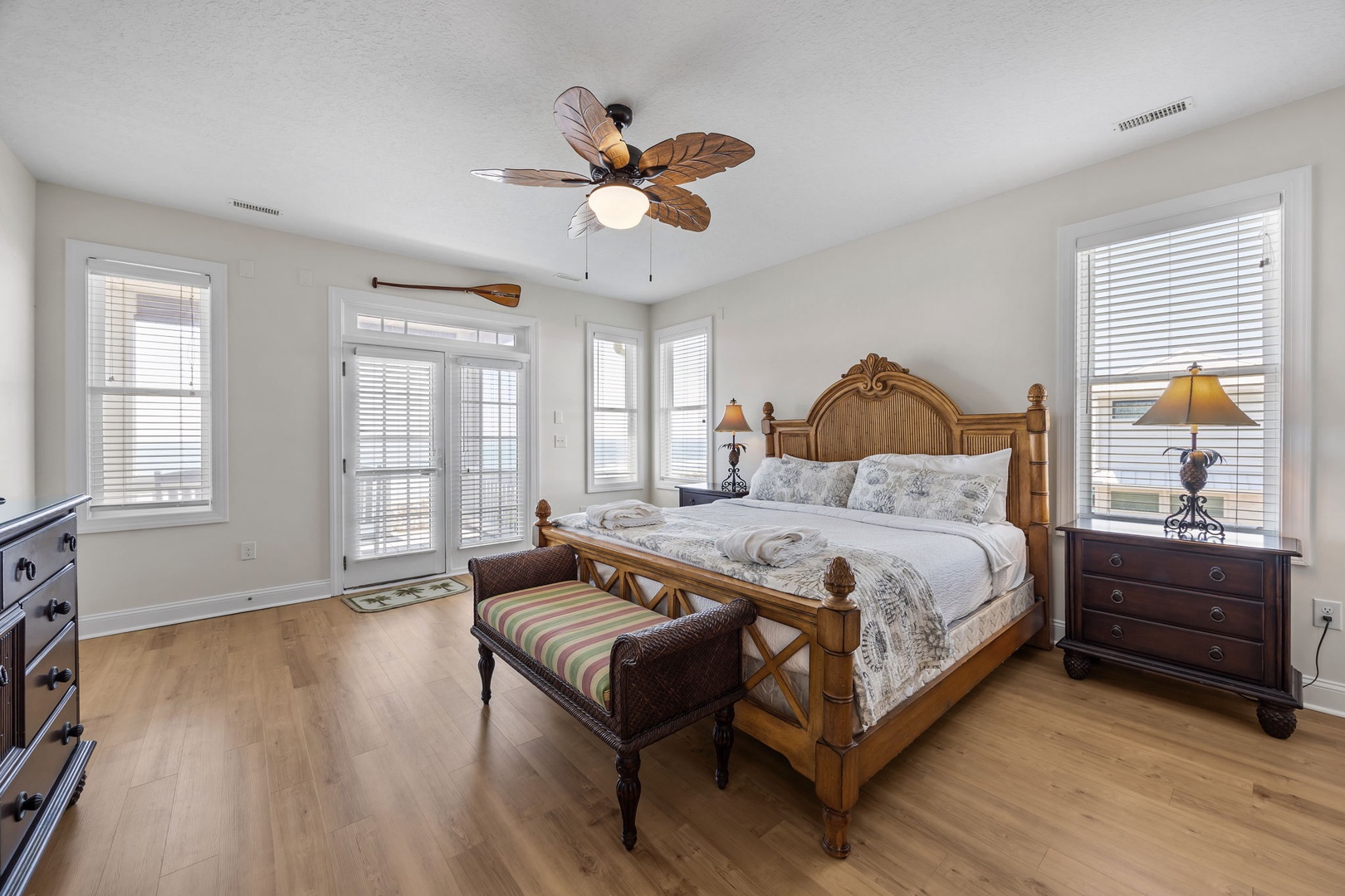 Drift off in your tropical bedroom featuring hardwood floors, bamboo-style bed, ceiling fan, and French doors opening to your private balcony.