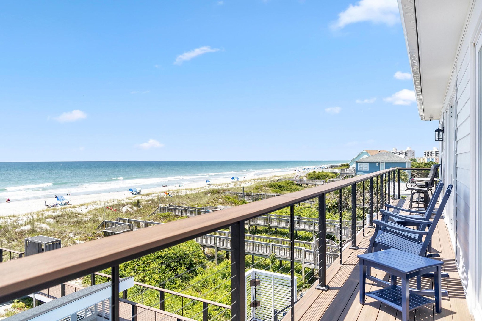 An expansive balcony overlooking the Atlantic coastline, complete with Adirondack chairs for leisurely mornings and sunset views. Sandy shores and coastal greenery stretch below.
