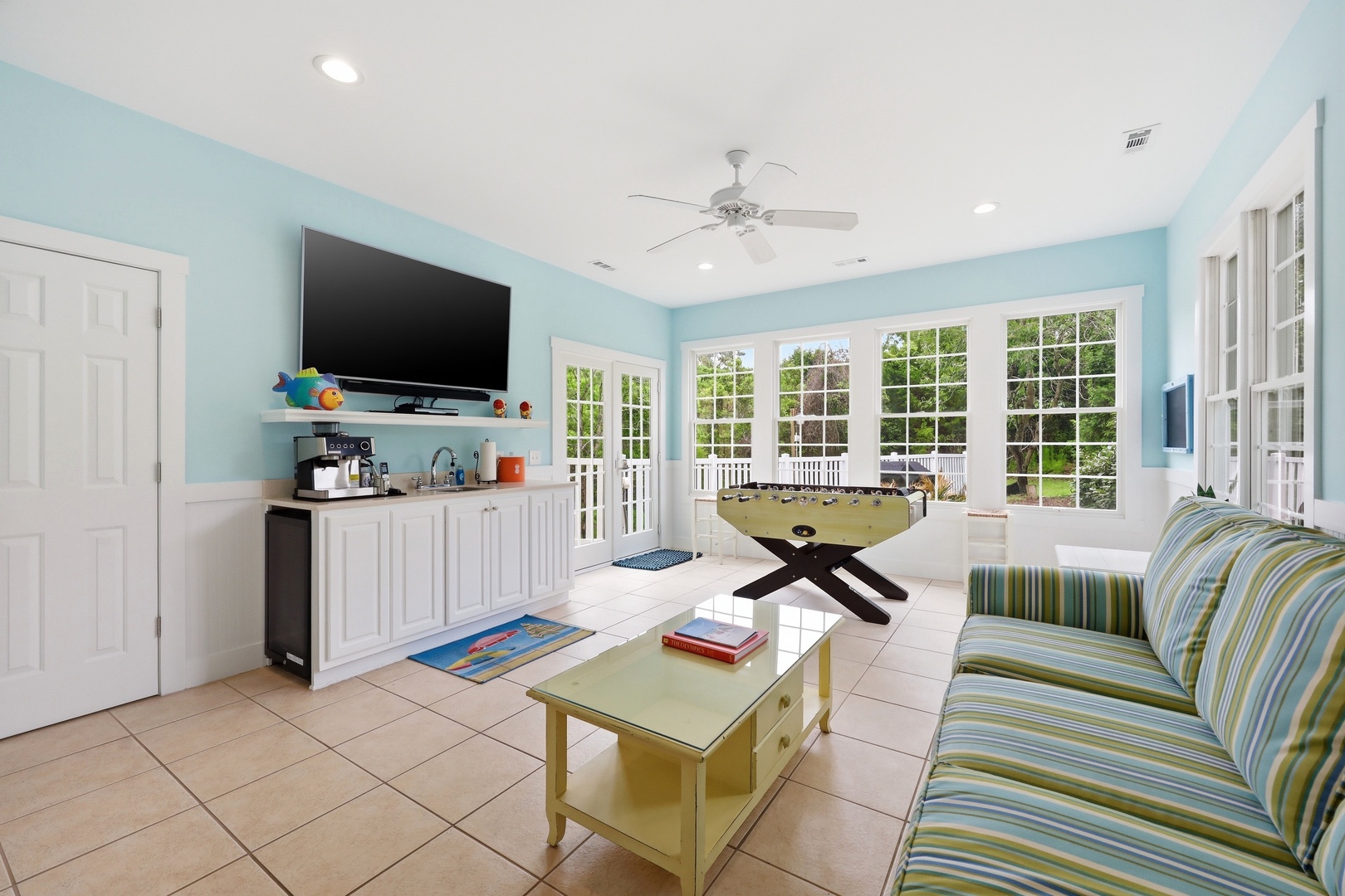 Unwind in your cheerful coastal lounge with comfy seating, entertainment center, and a foosball table for friendly competition. French doors open to the garden, flooding the space with natural light and fresh air.