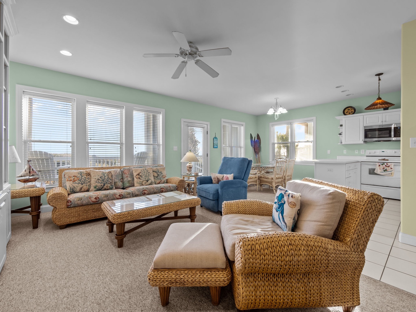 Relax in your spacious living room with coastal charm—wicker furniture, soothing green walls, and bright windows create the perfect beachside retreat.