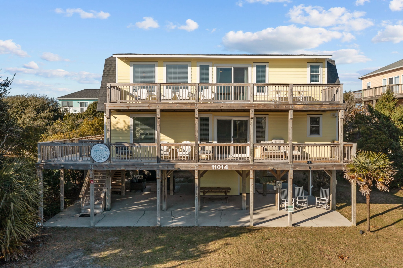 Three-story coastal house with multiple deck levels and covered parking in a peaceful neighborhood setting.