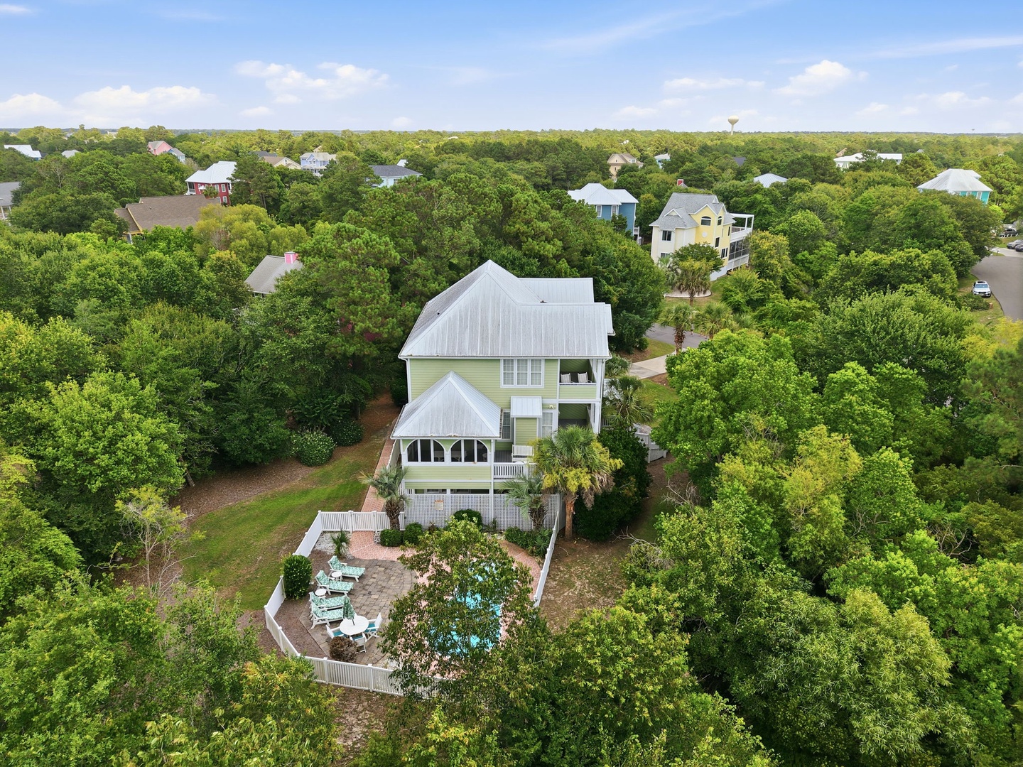 Aerial view of a charming coastal vacation rental nestled among lush greenery in a peaceful residential neighborhood, featuring a private patio and outdoor seating area.