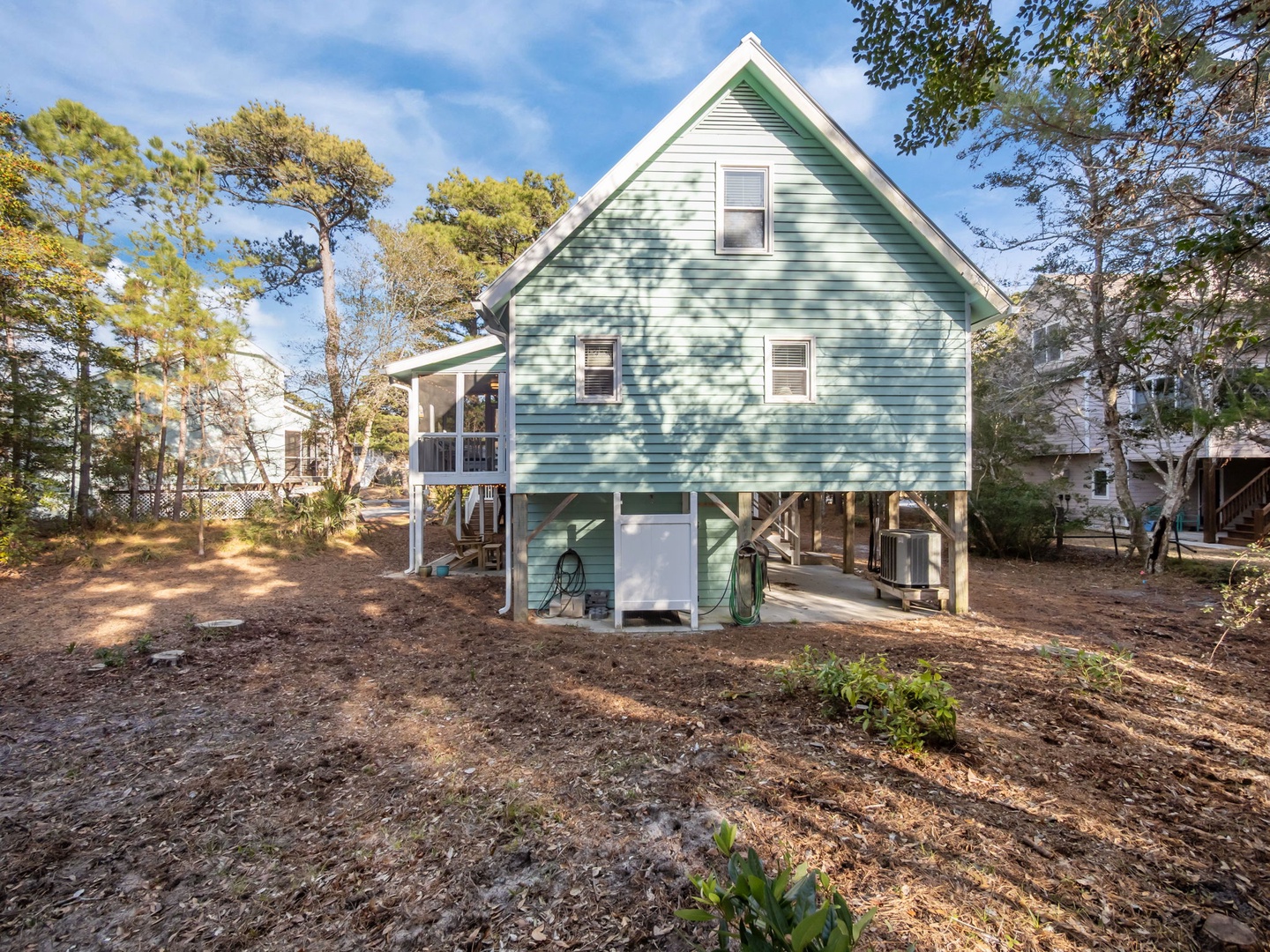 Charming coastal cottage with elevated design and enclosed parking sits among mature trees in a peaceful neighborhood setting.