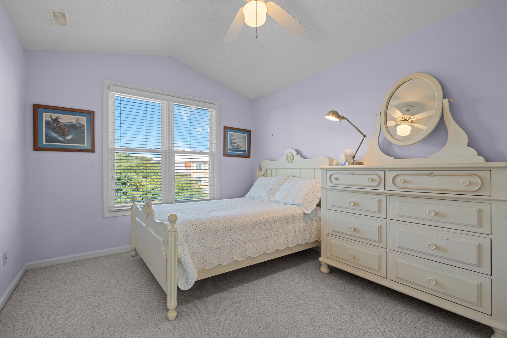Your peaceful bedroom retreat features soft lavender walls, cozy white linens, and charming nautical artwork that sets the perfect mood for restful nights.