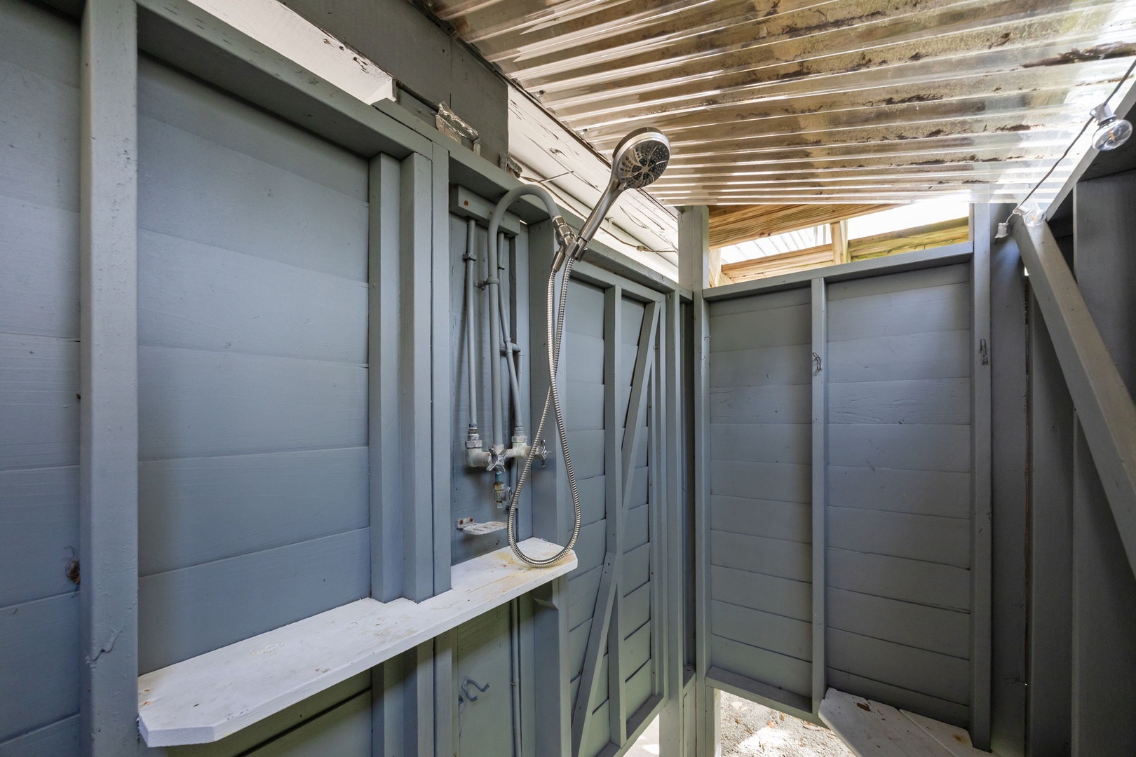 Step into your private outdoor shower sanctuary, where warm water meets cool sea breeze under rustic wooden beams.