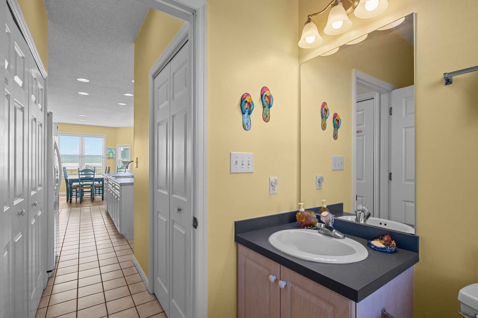 Bright yellow walls and cheerful flip-flop art create a welcoming bathroom space with convenient vanity and thoughtful amenities.