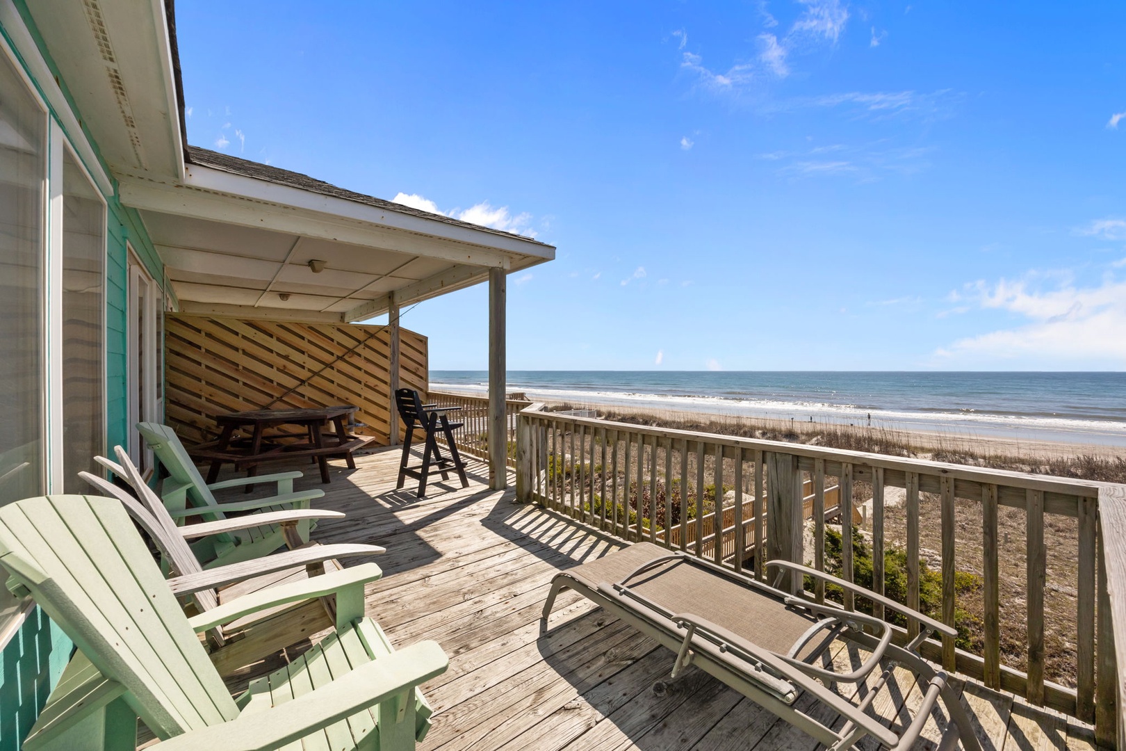 Beachfront deck with Adirondack chairs and dining table overlooking pristine sandy shores and endless ocean views.