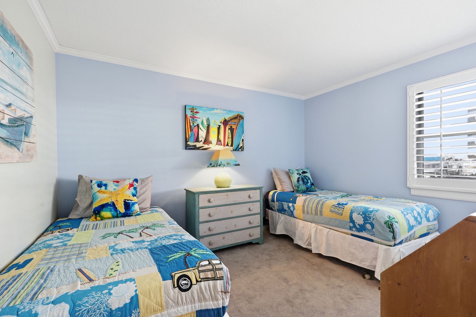 Your beachside bedroom features two twin beds with coastal-inspired bedding, soft blue walls, and cheerful surfboard artwork that sets a playful, relaxing vacation tone.