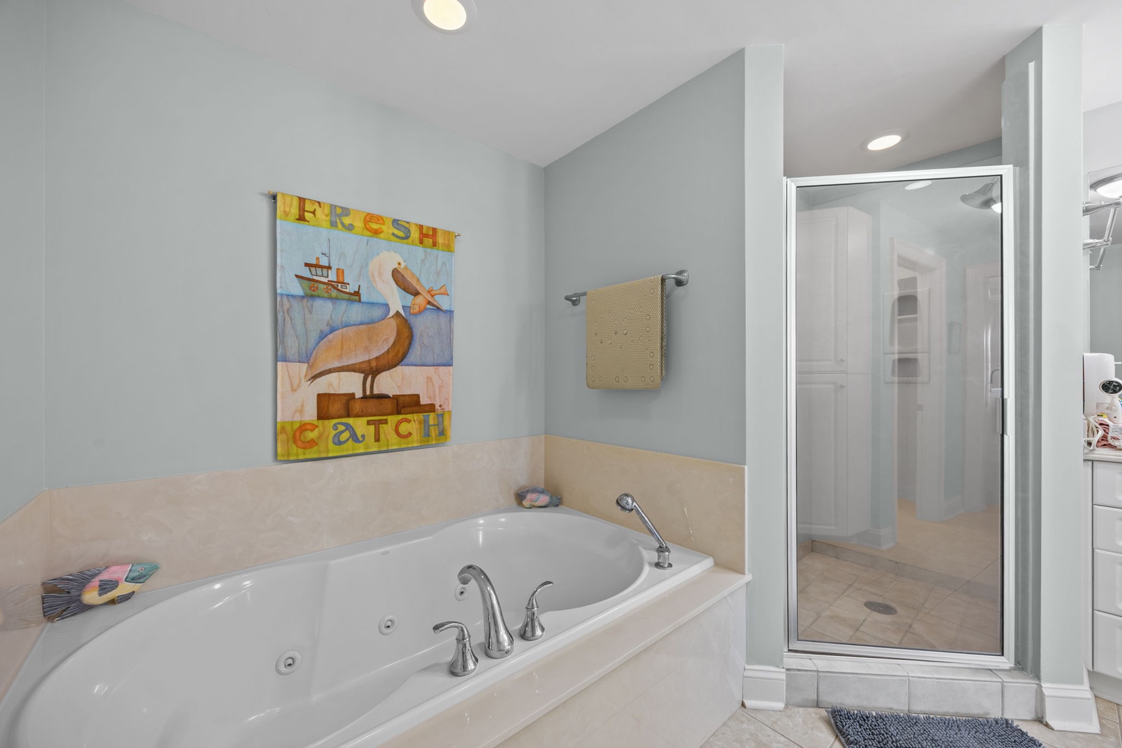 Unwind in your spa-like bathroom with a deep soaking tub and separate glass shower, complete with coastal artwork.