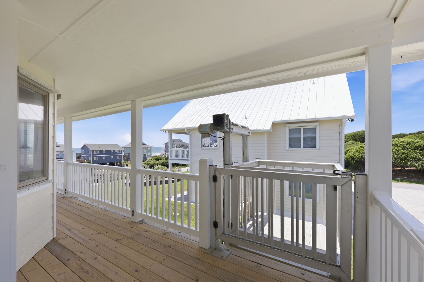 Covered deck with white railing offers a breezy outdoor retreat, perfect for morning coffee or evening relaxation while taking in the coastal neighborhood views.
