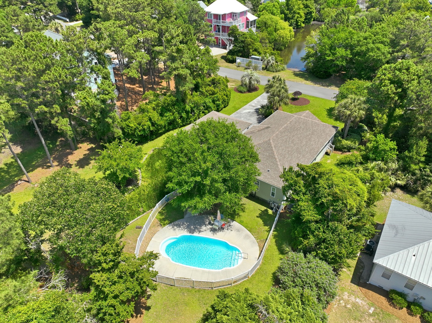 Aerial view of a serene rental home featuring a private backyard pool nestled among lush greenery and mature trees in a peaceful residential neighborhood.