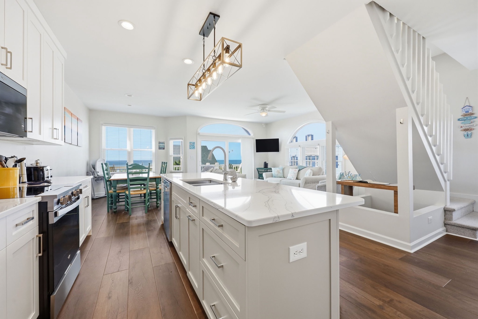 Your open-concept living space flows seamlessly from a chef's kitchen with marble countertops to a bright living area, all framed by stunning ocean views through arched windows.