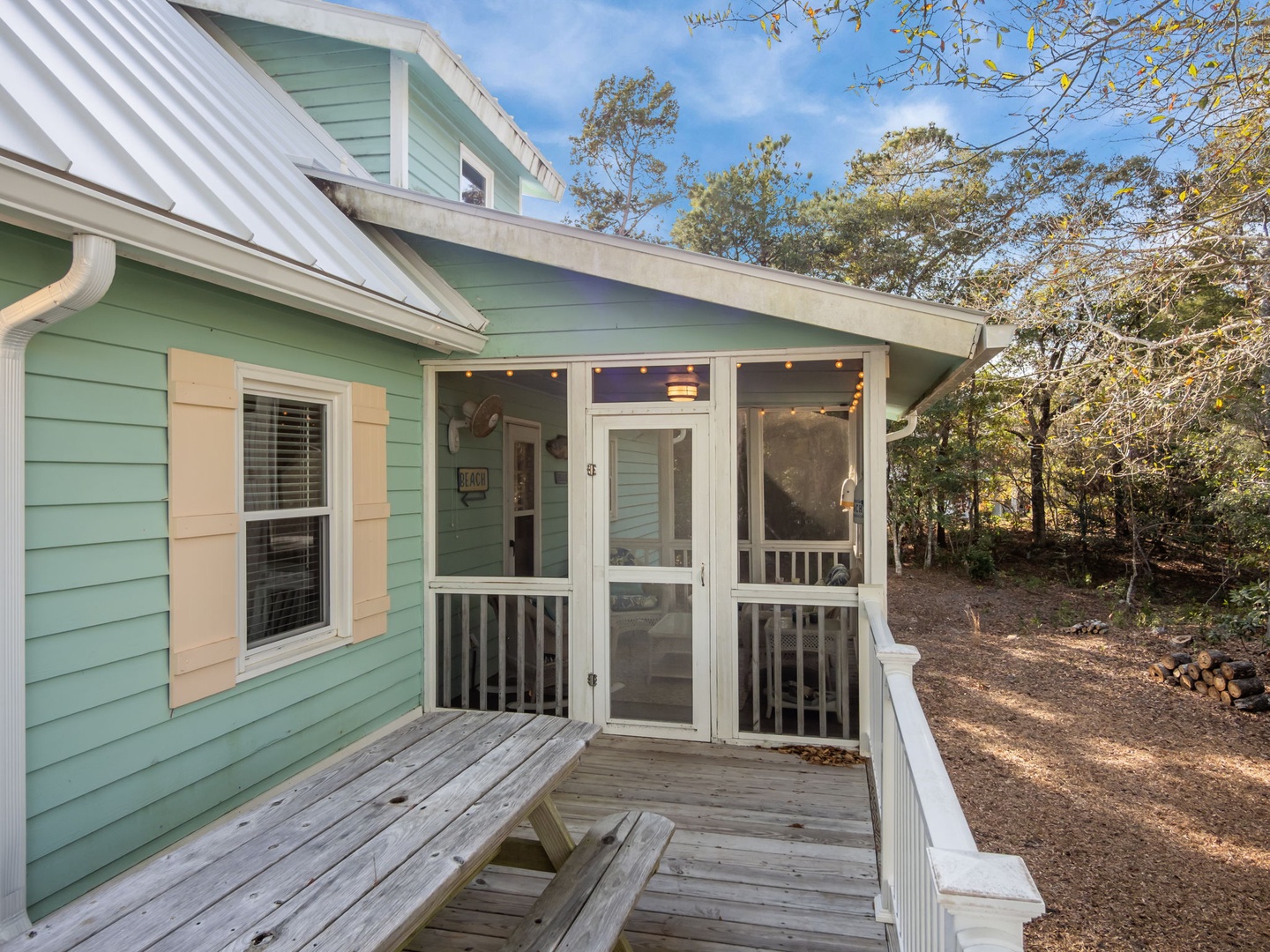 Charming coastal cottage with screened porch surrounded by mature trees in a peaceful wooded setting.