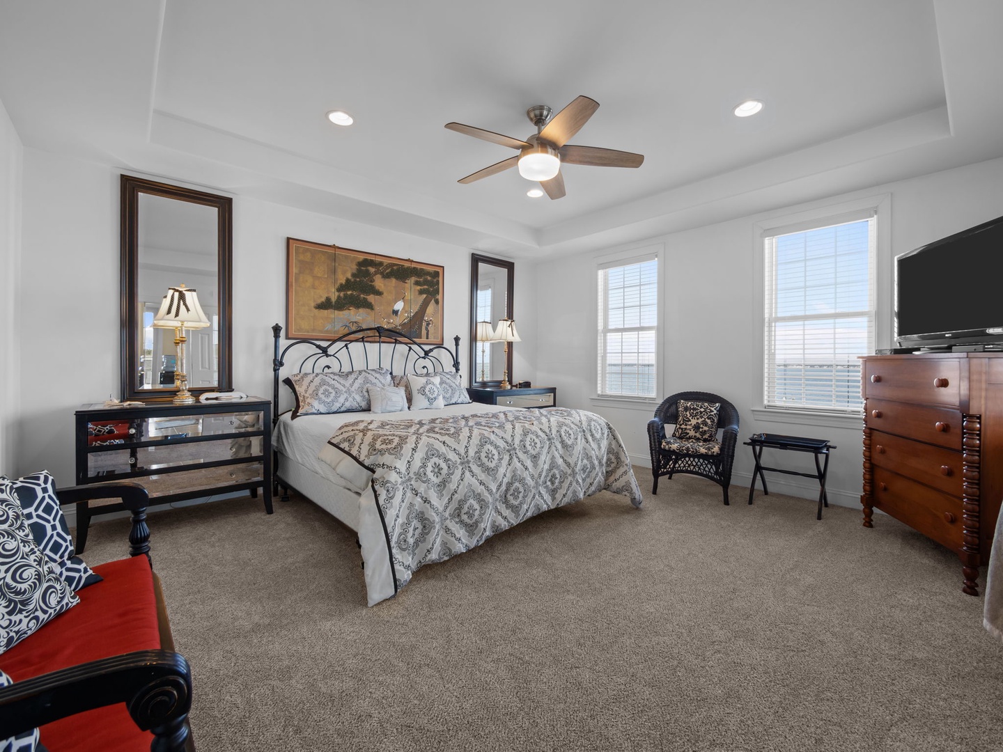 Relax in your elegant bedroom featuring a plush bed, ceiling fan, flat-screen TV, and natural light from two windows.