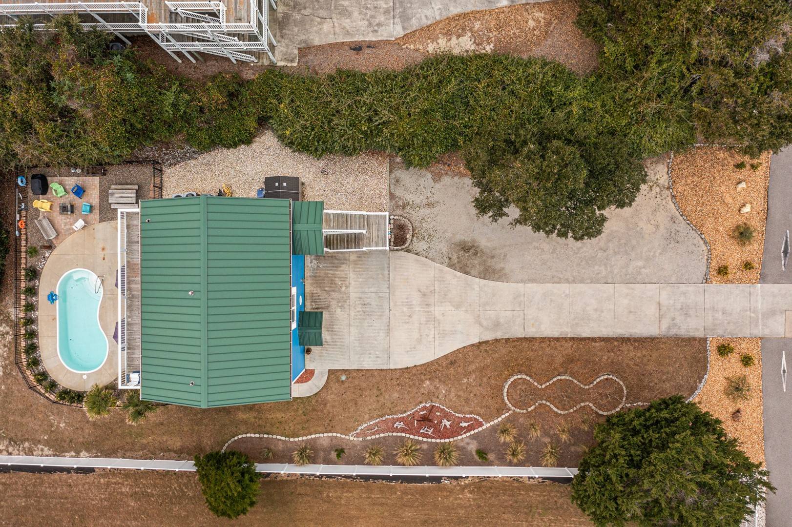 Aerial view showcasing the property's distinctive curved architecture, private pool, and beautifully landscaped grounds with mature trees and artistic pathway design.