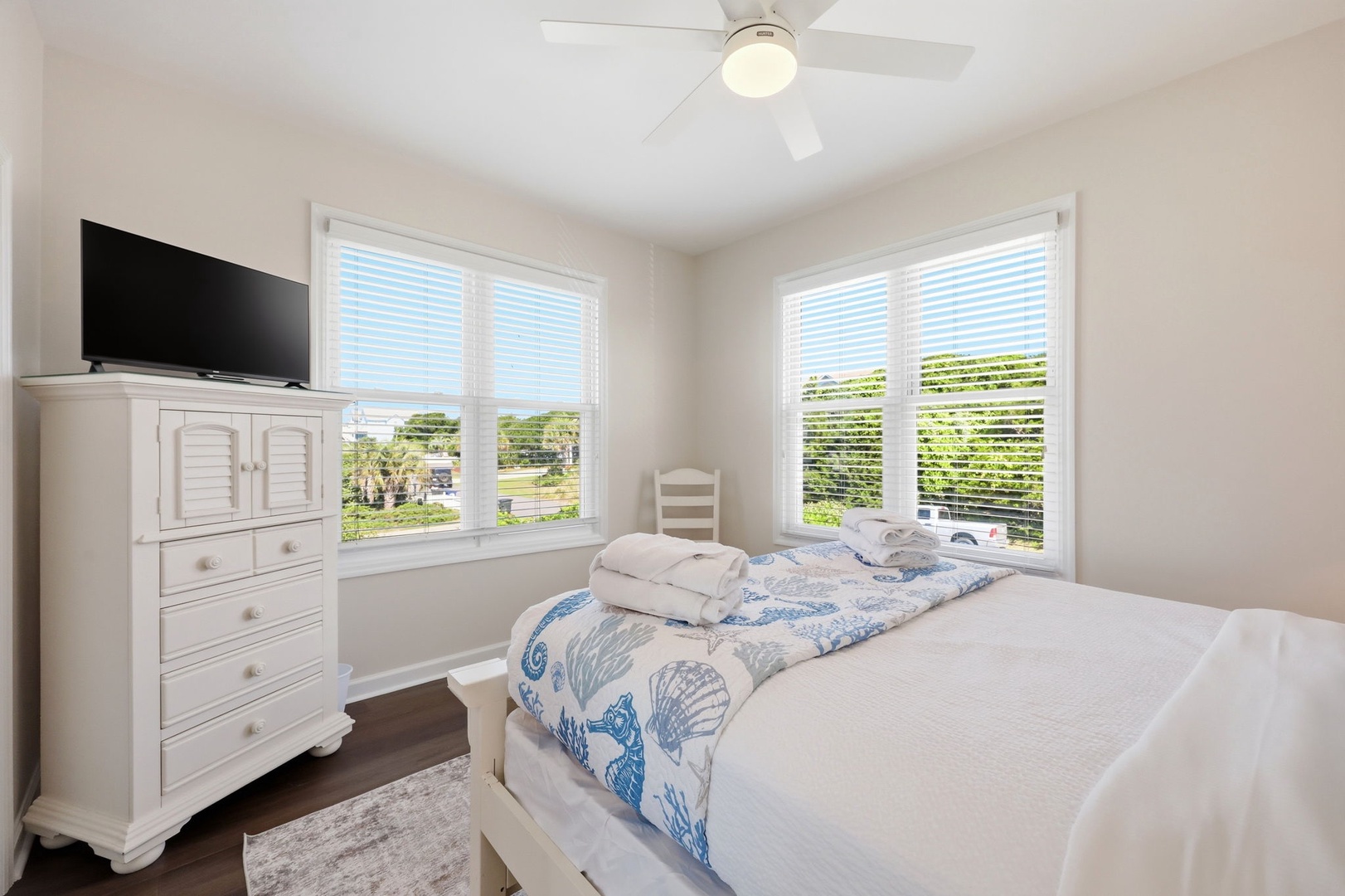 Settle into this serene bedroom where natural light frames peaceful views of the surrounding landscape. Your coastal retreat awaits with crisp linens, thoughtful beach-inspired touches, and a gentle ceiling fan overhead.