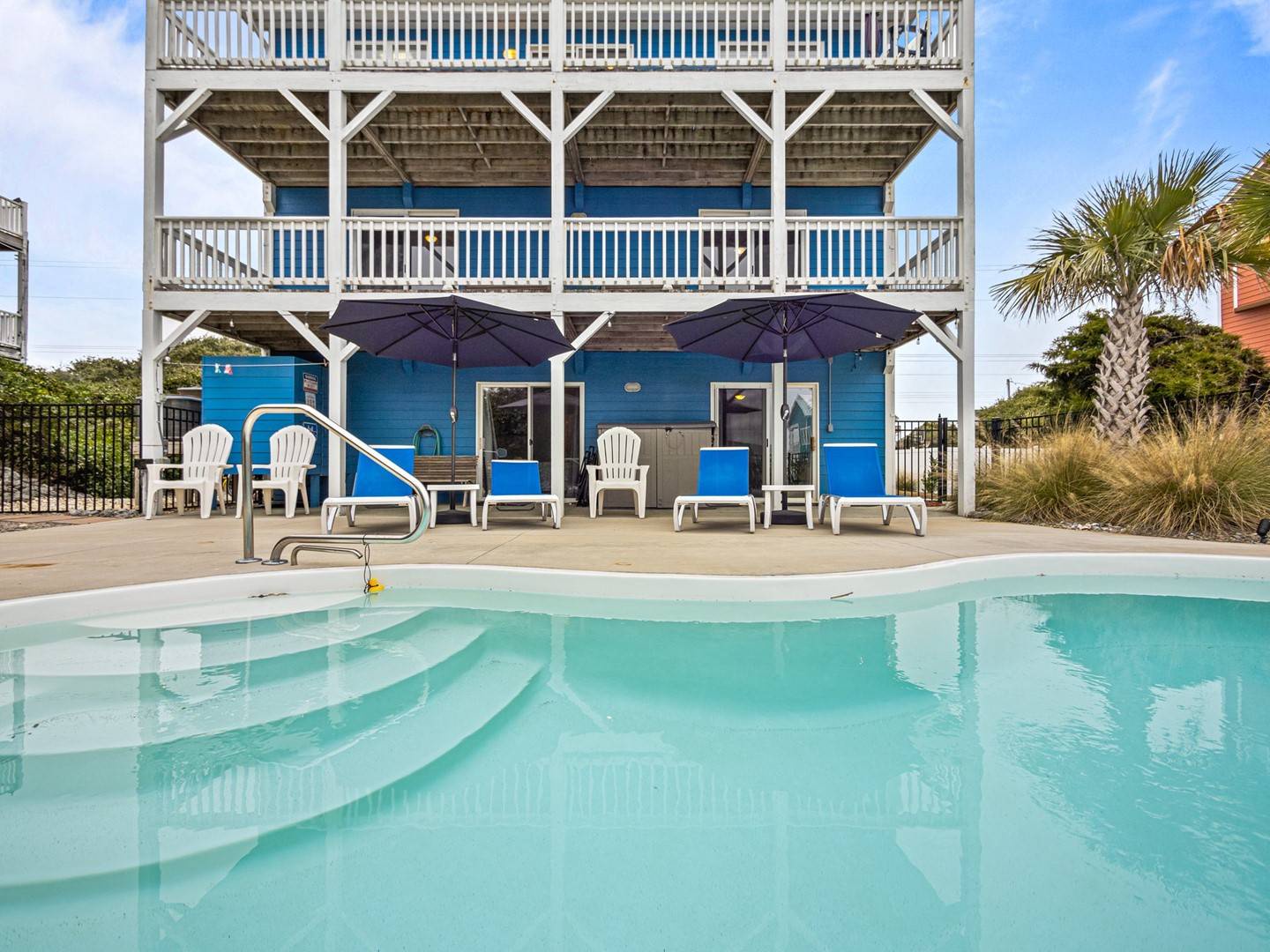 Dive into crystal-clear waters steps from your bright blue beach house with multiple decks and poolside lounging.