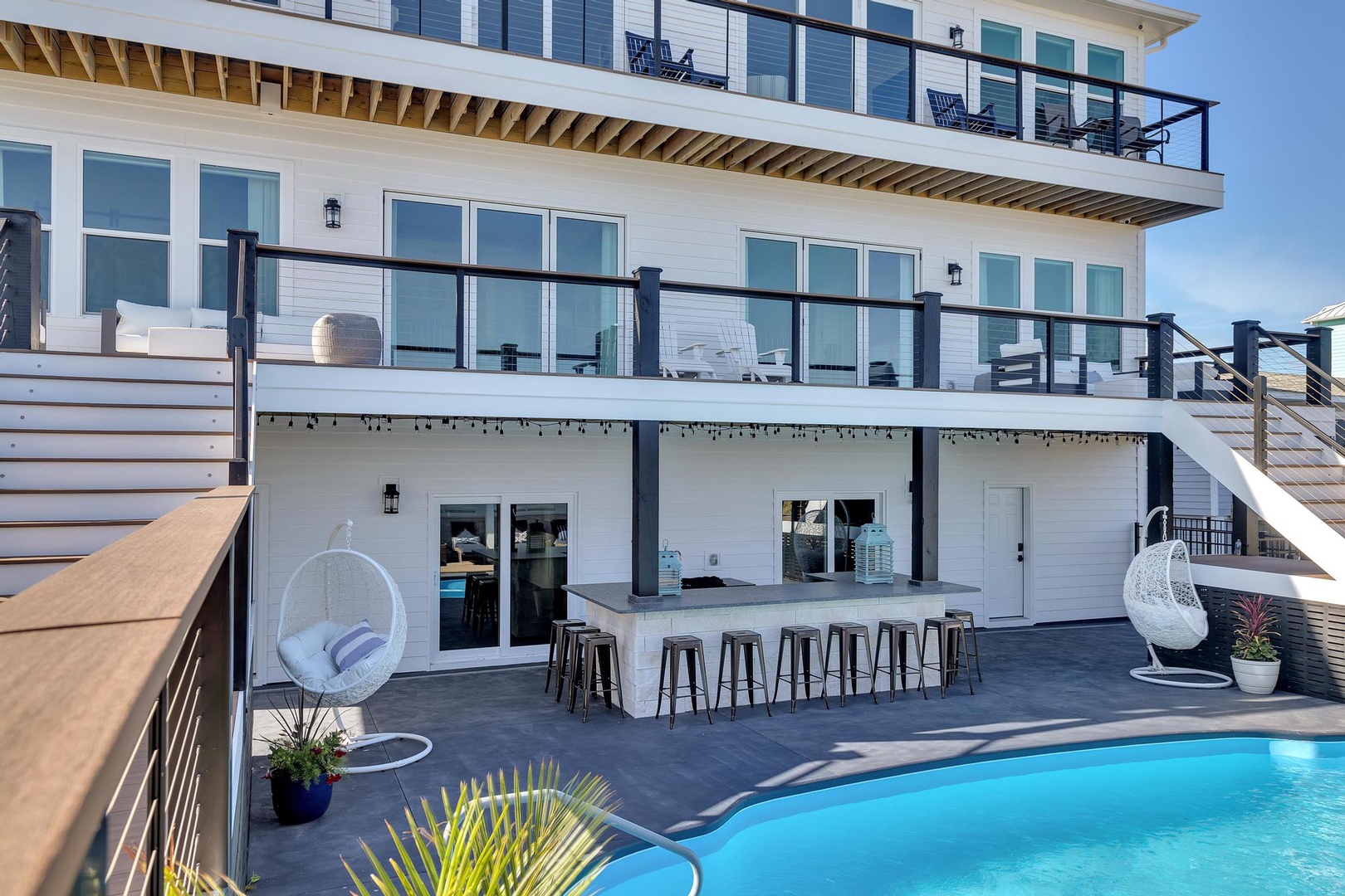 This multi-level beachfront property features expansive balconies, a sparkling pool, and an outdoor bar—perfect for your ultimate coastal getaway with friends and family.