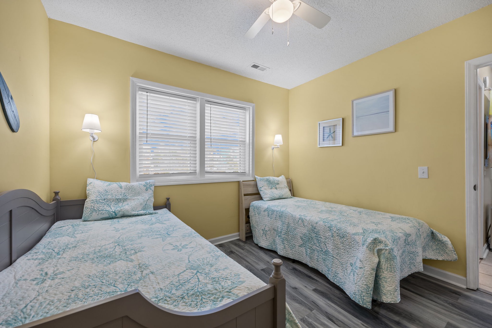 Twin beds dressed in coastal-inspired linens create the perfect spot for restful sleep beneath warm yellow walls and gentle ceiling fan breezes.