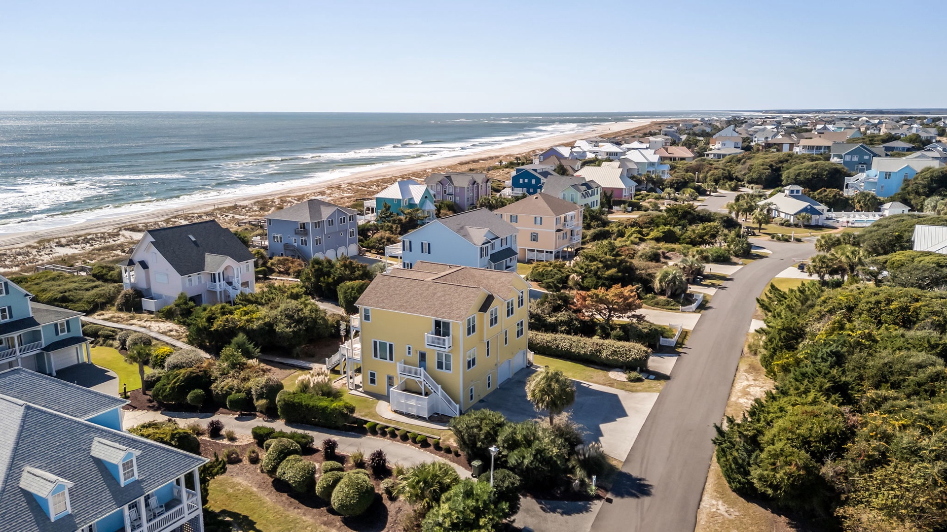 Aerial view of coastal beach community with vacation homes nestled among trees near sandy shoreline.
