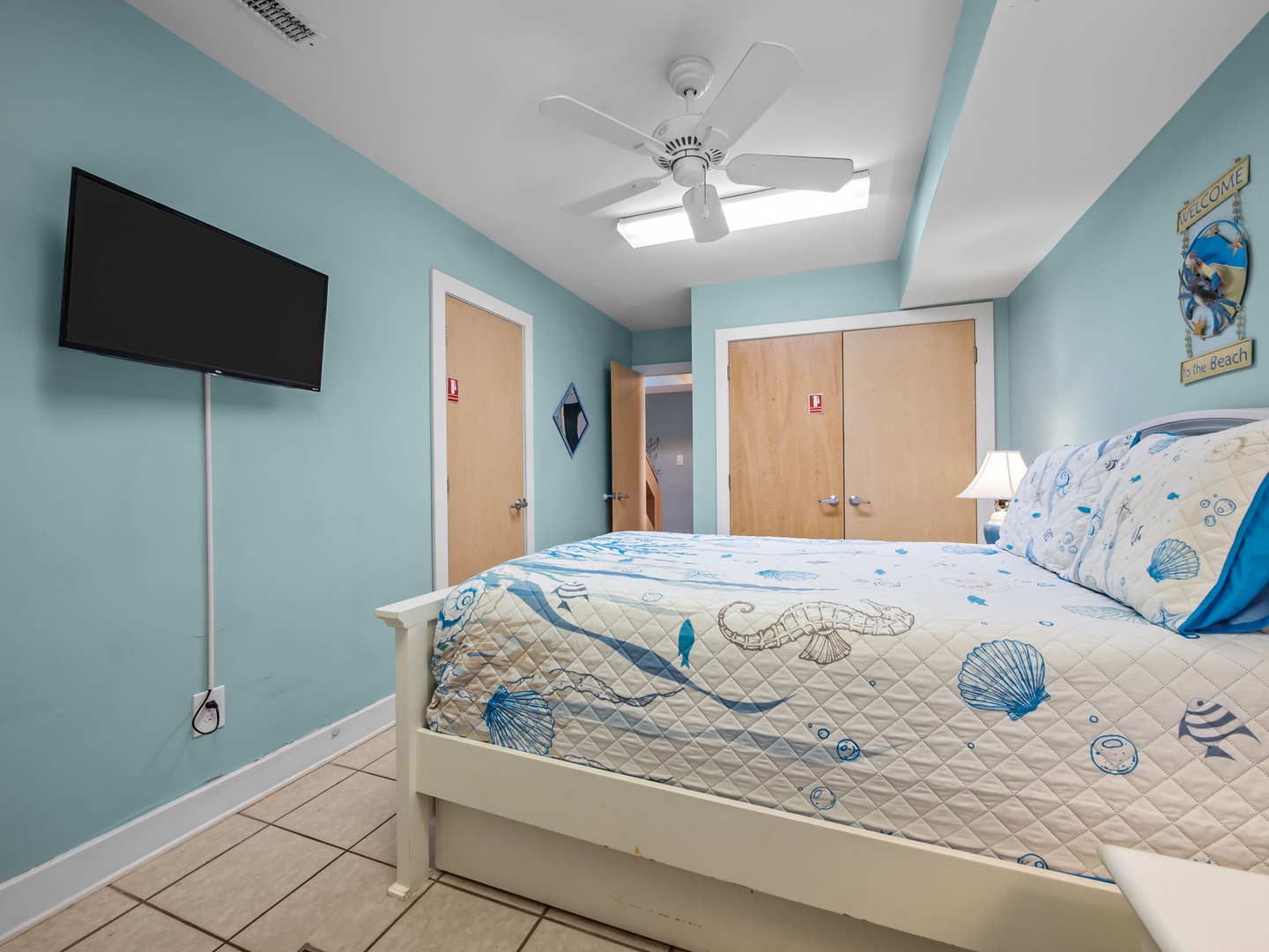 Your coastal-themed bedroom offers serene ocean vibes with sea-blue walls, charming shell bedding, and gentle ceiling fan breezes for ultimate relaxation.