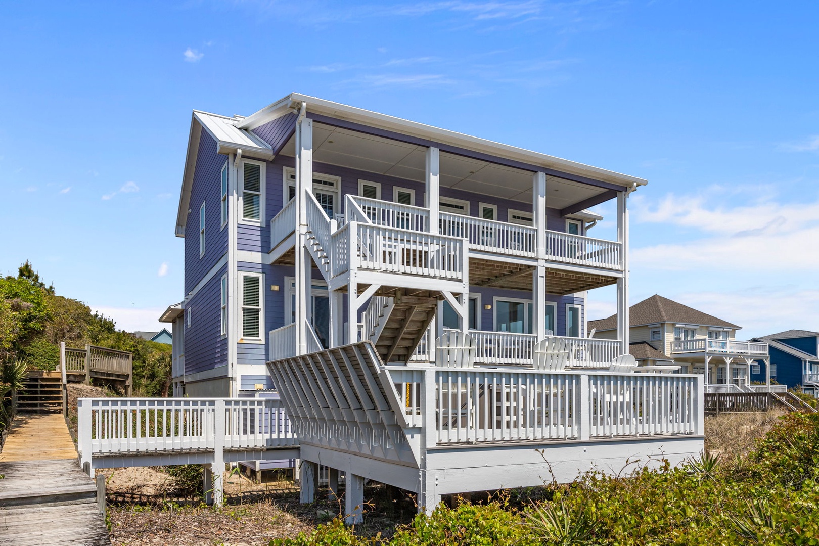 Charming coastal home with wraparound balconies and ocean access, nestled among neighboring beach houses under clear blue skies.