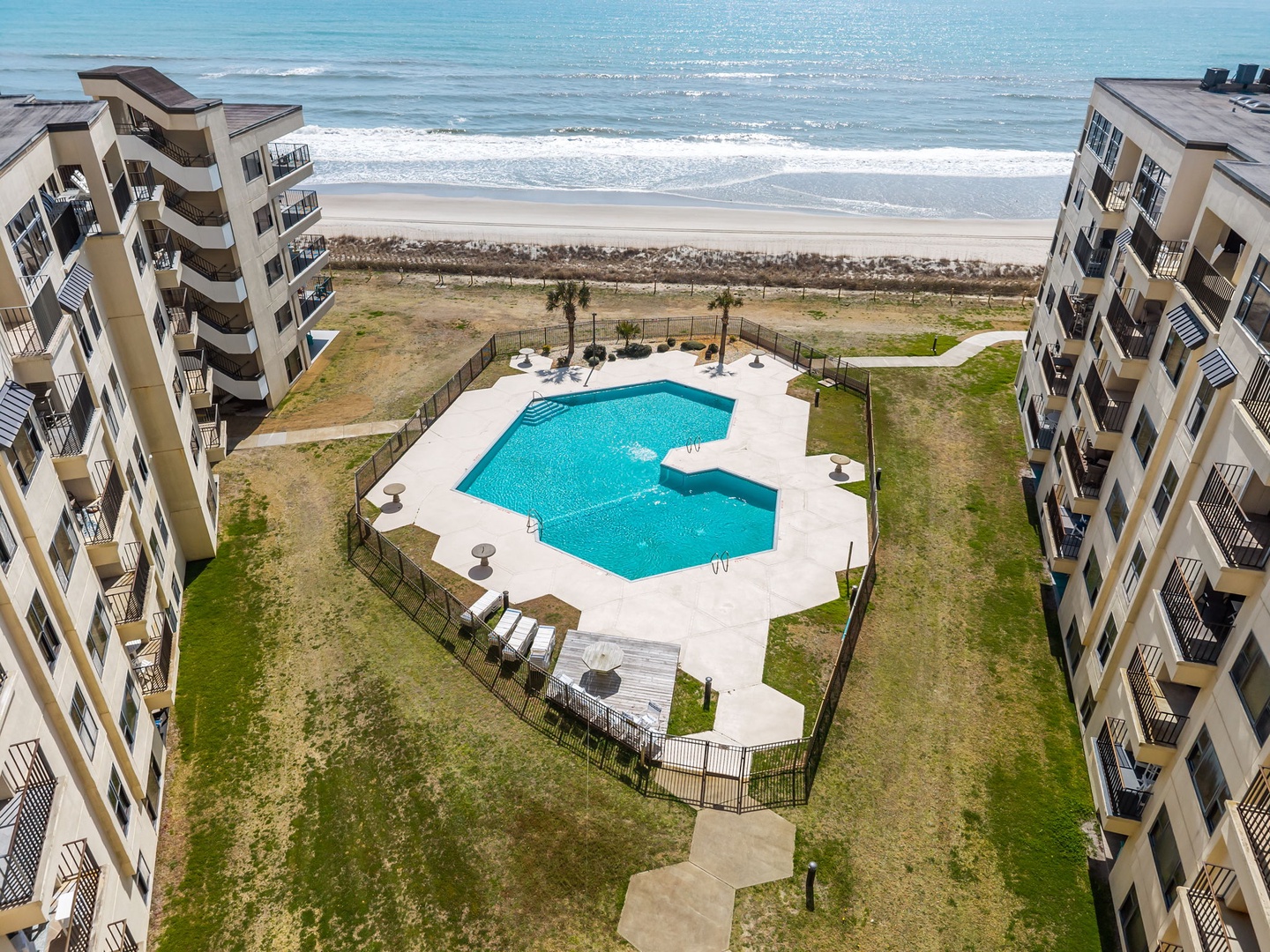 Beachfront property with direct access to sandy shores, featuring a sparkling pool nestled between multi-story buildings with private balconies overlooking the ocean.