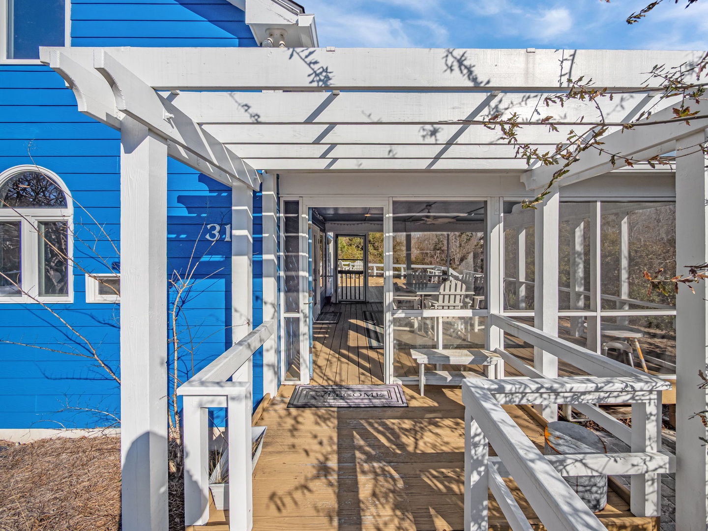 Charming blue cottage entrance with white pergola-covered deck creates your perfect coastal retreat arrival experience.